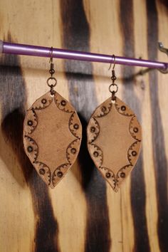 a pair of wooden earrings hanging from a hook on a wall with a purple handle