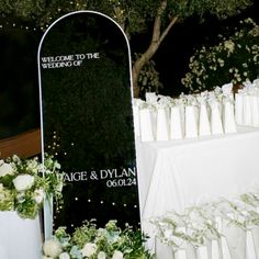 a sign that is sitting in front of some flowers and candles on a table with white linens