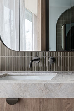 a bathroom sink with two faucets in front of a mirror and curtained window