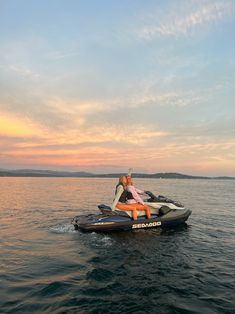 two people riding on the back of a jet ski in the middle of water at sunset