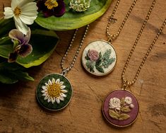 three necklaces with flowers on them sitting next to a potted plant and flowerpot