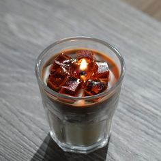 a glass filled with liquid sitting on top of a wooden table next to a lit candle