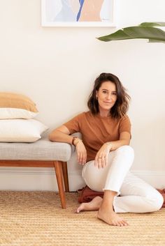 a woman sitting on the floor in front of a couch with pillows and a plant