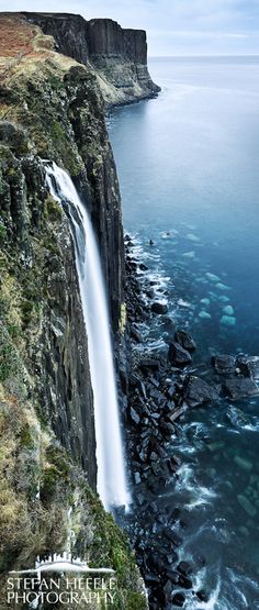 a large waterfall flowing into the ocean next to a cliff