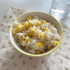 a bowl filled with rice and corn sitting on top of a table next to a glass of water