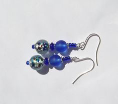 These earrings are made with gorgeous vintage foil glass beads with blues, greens, aquas, and amber speckles that have been combined with deep blue matte glass beads and accented with glittery royal blue seed beads. Hanging Length: 2 inches. Ear wires: silver plated surgical steel. Blue Round Beaded Earrings With Spacer Beads, Blue Earrings With Spacer Beads For Gift, Blue Czech Glass Beaded Earrings With Dangling Beads, Blue Czech Glass Beaded Earrings, Blue Glass Earrings With Dangling Beads, Blue Round Bead Glass Earrings, Blue Glass Round Bead Earrings, Blue Glass Round Beads Earrings, Blue Glass Beaded Earrings With Ear Wire