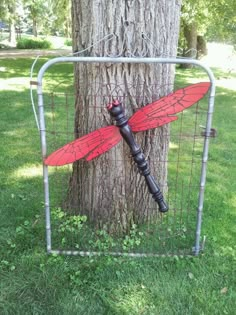 a red dragonfly is attached to the side of a metal fence next to a tree