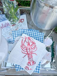 a table topped with plates and napkins covered in red lobster artwork next to a vase filled with flowers