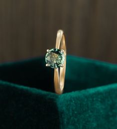 an engagement ring with a green stone in the center on a velvet display case,