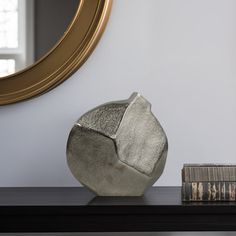 a silver vase sitting on top of a black table next to a bookshelf