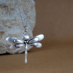 a silver dragonfly necklace sitting on top of a rock