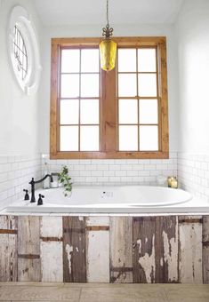 a bath tub sitting under a window next to a wooden sink faucet in a bathroom