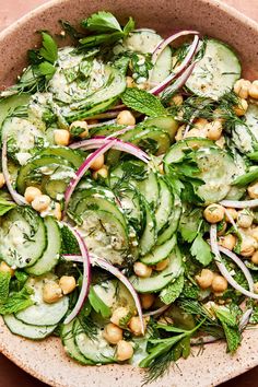 a bowl filled with cucumber, chickpeas and herbs on top of a table