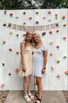 two women standing next to each other in front of a wall with flowers on it