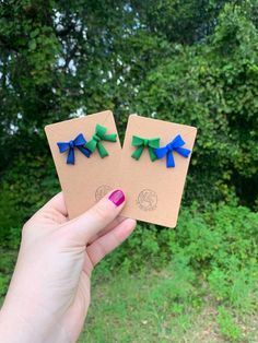 two pieces of paper with blue and green bows are held up in front of some trees