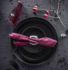 a black plate topped with a pink napkin next to utensils and a bottle