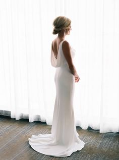 a woman standing in front of a window wearing a white dress