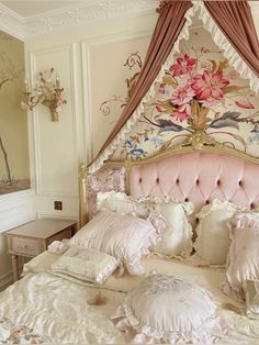 a fancy bed with pink and gold decor in a white walled room, decorated with flowers on the headboard