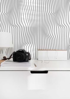 a camera sitting on top of a table next to a lamp and some books in front of a striped wall