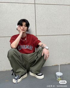 a young man sitting on the ground next to a wall talking on a cell phone