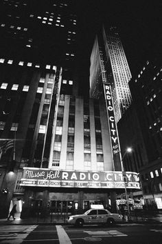 the radio city building is lit up at night in black and white, with cars driving by