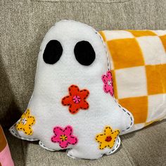 a white stuffed ghost sitting on top of a couch next to a checkered pillow