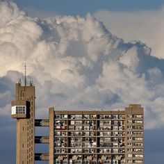 black and white photograph of an apartment building in front of a large cloud filled sky