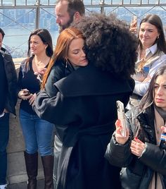 two women hugging each other in front of a group of people on top of a building