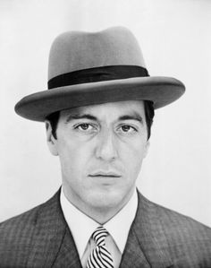 a man in a suit and tie with a hat on his head, looking at the camera