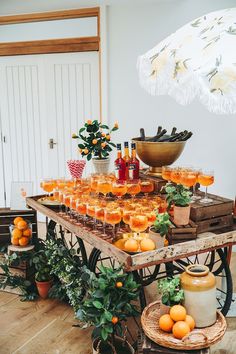 a table topped with lots of glasses filled with oranges next to potted plants