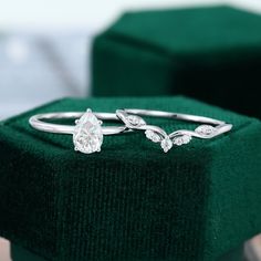 two wedding rings sitting on top of a green velvet ring box, with one diamond set in the middle