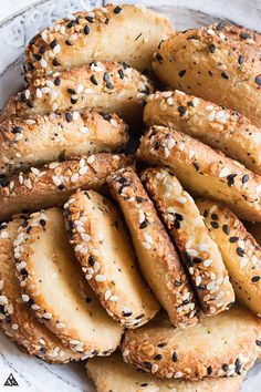 sesame seed bagels piled on top of each other in a white plate with black sesame seeds