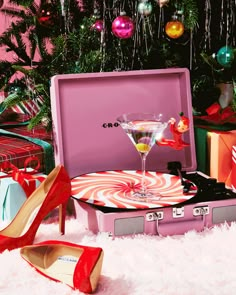 a pink suitcase sitting on top of a snow covered ground next to christmas trees and presents