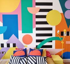 a bed with pillows on it in front of a colorful wall