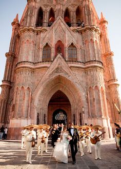 a bride and groom are walking in front of an old building with people holding umbrellas