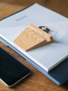 a wooden object sitting on top of a book next to a cell phone and tablet