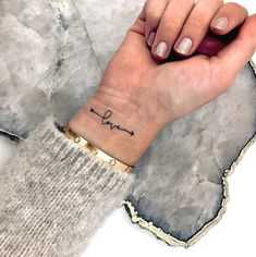 a woman's wrist tattoo with the word love written in cursive writing