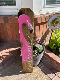 a wooden sign with a pink flamingo painted on it next to a potted plant