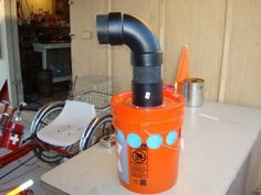 an orange bucket with a pipe sticking out of it sitting on a table next to a bike