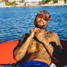 a man with tattoos sitting in a boat on the water