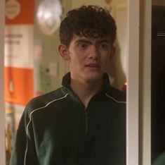 a young man standing in front of a mirror wearing a green sweater and black pants