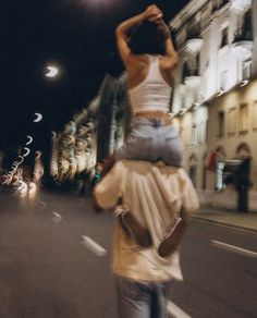 a man carrying a woman on his back in the middle of an empty street at night