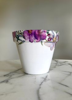 a white bowl with purple flowers painted on the side sitting on a marble countertop