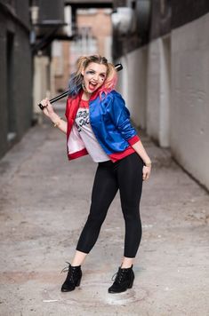 a woman in black pants and a blue jacket holding a baseball bat on her shoulder