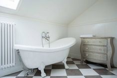 a white bath tub sitting next to a wooden dresser in a bathroom with black and white checkered flooring