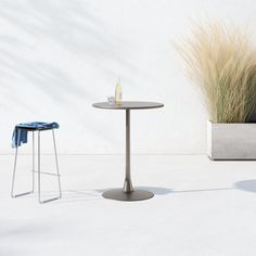 an outdoor table and two stools in front of a white wall