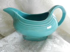 a teal colored pitcher sitting on top of a white table cloth with lace in the background