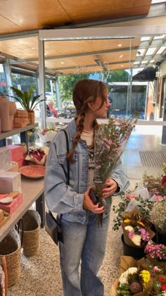 a woman standing in front of a flower shop holding flowers