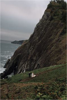 a bride and groom standing on top of a hill next to the ocean with cliffs in the background