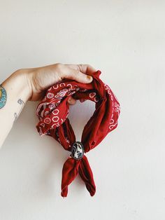 a woman's hand holding a red bandana on top of a white wall